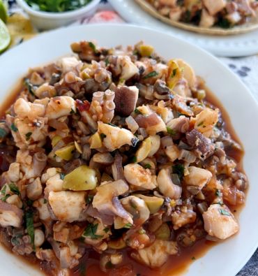 Imagen de un exquisito plato de Pulpo al Ajillo, servido con ajos dorados en aceite de oliva y decorado con perejil fresco. El pulpo está tierno y jugoso. Este plato tradicional es una deliciosa opción de mariscos con un toque mediterráneo